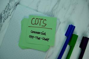 COTS- Commercial Off-The-Shelf write on sticky note isolated on Wooden Table. Business Concept photo