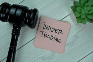 Concept of Insider Trading write on sticky notes with gavel isolated on Wooden Table. photo