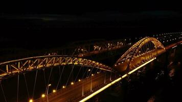 brilhante luzes, pontes com arcos, noite cidade. uma estrada ponte através a rio, ocupado a partir de uma drone. video