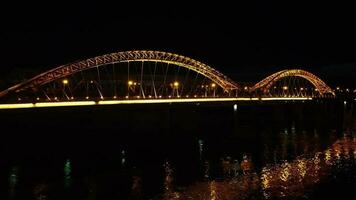 brilhante luzes, pontes com arcos, noite cidade. uma estrada ponte através a rio, ocupado a partir de uma drone. video