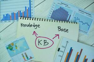 Concept of Knowledge Base write on a book with statistics isolated on Wooden Table. photo