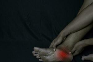 Asian Man Holding his foot. He feels pain foot heel with black background. Plantar Fascilitis. Medical or healthcare concept photo