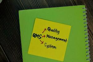 QMS - Quality Management System write on sticky notes isolated on Wooden Table. photo