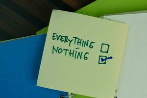 Everything and Nothing write on sticky notes and supported by additional services write on a sticky notes isolated on Wooden Table. photo