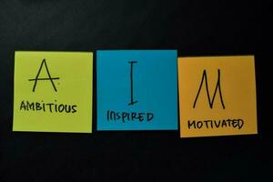 AIM - Ambitious Inspired Motivated write on sticky notes isolated on office desk. photo