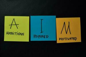 AIM - Ambitious Inspired Motivated write on sticky notes isolated on office desk. photo