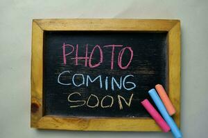 Photo Coming Soon write on a chalkboard isolated on wooden table.