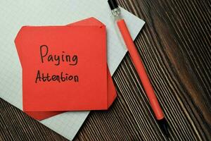 Paying Attention write on sticky note isolated on Wooden Table. Financial Concept photo