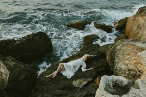 mujer en un blanco vestir acostado en un Roca en un blanco vestir vacaciones concepto foto