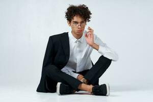 stylish young man with curly hair and in a classic suit on a light background indoors in full growth photo