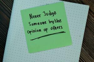 Never judge someone by the opinion of others write on sticky notes isolated on Wooden Table. Motivation concept photo