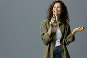 disfruté Rizado hermosa mujer en casual caqui verde camisa sostener botella bebida limpiar agua cerca ojos posando aislado en terminado gris azul antecedentes. sano estilo de vida. agua es vida concepto. Copiar espacio foto