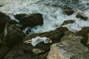 attractive woman with long hair lying on rocky coast with cracks on rocky surface vacation concept photo