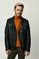 blond man in orange sweater and leather jacket on light background cropped view photo