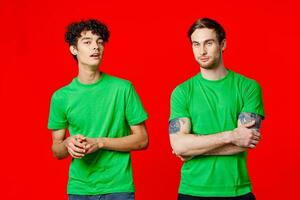 two men in green t-shirts are standing next to friendship red background photo