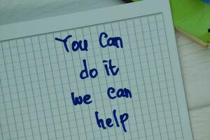 You can Do It We Can Help write on a book isolated on Wooden Table. photo