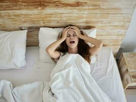 emotional woman with open mouth hold hands on head while lying in bed top view photo