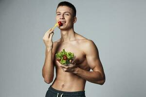 alegre chico con un bombeado arriba cuerpo un plato de ensalada sano comida frescura energía rutina de ejercicio foto