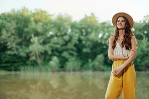 un joven mujer en un hippie Mira viajes en naturaleza por el lago vistiendo un sombrero y amarillo pantalones en el otoño foto