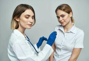 contento mujer médico en azul guantes y hembra paciente en blanco camiseta estetoscopio médico vestido foto