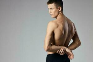 a man with pumped up muscles holds his hands behind his back on a gray background and behind Model photo