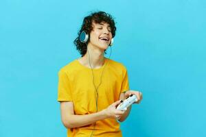 curly guy plays with joystick in yellow t-shirts blue background photo