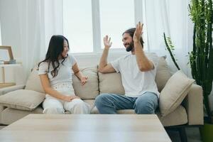 A man and a woman sitting at home on the couch in white stylish t-shirts and chatting merrily smiling and laughing at home. Male and female friendship photo