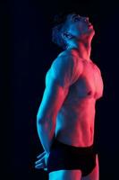 sexy man with a pumped-up torso posing on a dark background side view photo