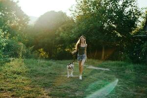 un mujer carreras con un perro en el bosque durante un noche caminar en el bosque a puesta de sol en otoño. estilo de vida Deportes formación con tu amado perro foto