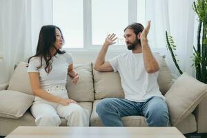 A man and a woman sitting at home on the couch in white stylish t-shirts and chatting merrily smiling and laughing at home. Male and female friendship photo