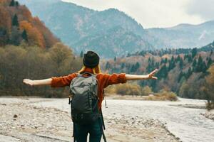 a traveler with a backpack in a sweater and jeans are resting in the mountains in nature near the river in autumn photo