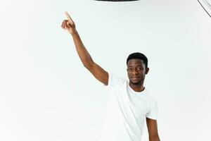 African American in a white t-shirt and beige trousers gesturing with his hands on a light background photo