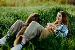 Woman game with her dog in nature smiling and lying on the green grass in the park, happy healthy relationship between mistress and pet photo