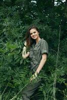 woman in forest in overalls, touches hair with his hands on his head green leaves photo