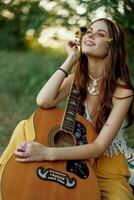 Hippie eco friendly woman with a guitar relaxing in nature sitting on a plaid by the lake in the evening in the rays of the setting sun. A lifestyle in harmony with the body and nature photo