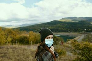 woman hiker resting in the mountains in the autumn forest with a medical mask on her face photo