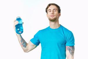 athlete in a blue t-shirt with a bottle of water on a white background and a tattoo on his arm photo