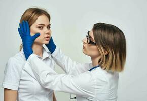 mujer médico en un médico vestido y en azul guantes con un estetoscopio alrededor su cuello y un hembra paciente foto