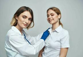 contento mujer médico en azul guantes y hembra paciente en blanco camiseta estetoscopio médico vestido foto