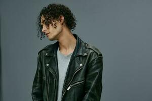 Handsome stylish tanned curly man leather jacket looks aside posing isolated on over gray studio background. Cool fashion offer. Huge Seasonal Sale New Collection concept. Copy space for ad photo