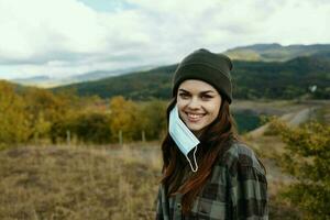 retrato de contento mujer con médico máscara en el oído y naturaleza montañas otoño foto