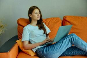 portrait of a woman chatting on the orange couch with a laptop Lifestyle photo