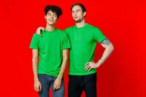 two men in green t-shirts are standing side by side communication isolated background photo