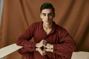 Nice guy in a brown shirt with a mirror on the table and a fabric background photo