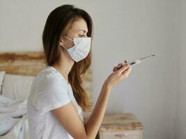 woman in medical mask with thermometer in hands checking temperature health photo