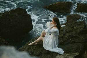 hermosa mujer en blanco vestir mojado pelo Roca playa nublado clima foto