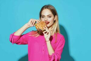 cheerful blonde in a pink shirt hamburger fast food snack blue background photo