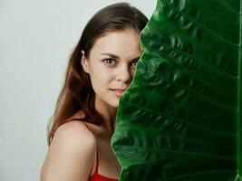 woman in red swimsuit green leaf cover her face close-up studio photo