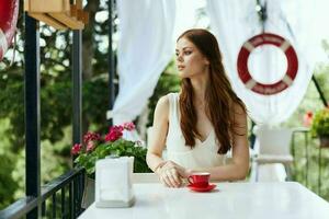 Young stylish woman in a white dress drinks coffee outdoors in a cafe Happy female relaxing photo