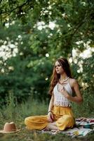 un joven hippie mujer medita en naturaleza en el parque, sentado en un loto posición en su vistoso tartán y disfrutando armonía con el mundo en ropa ecológica en el otoño foto